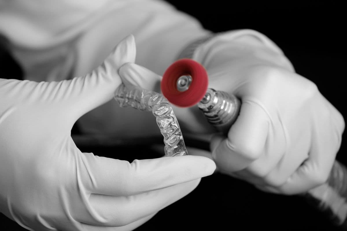 A clear dental aligner being finished by gloved hands